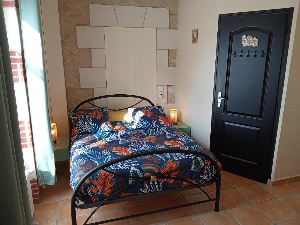 a bedroom with a bed with a colorful comforter and a door at Le Relais du Jardin in Orbigny