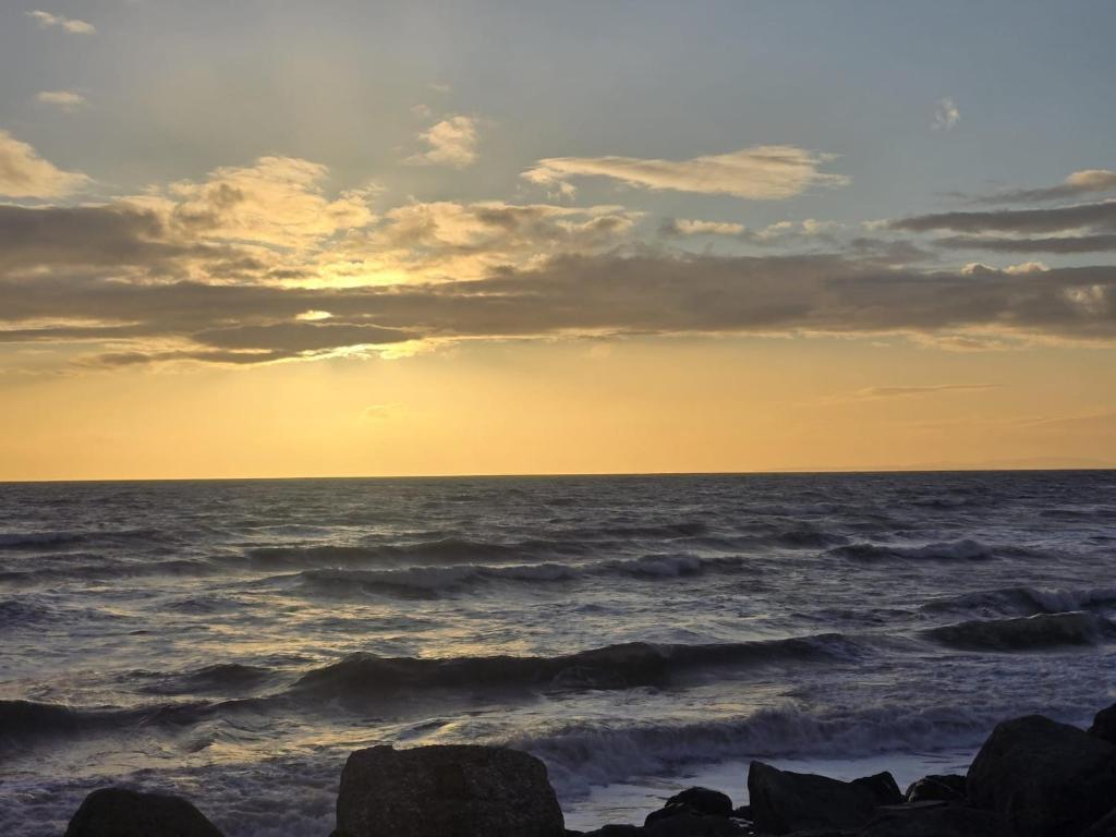 a sunset over the ocean with rocks on the beach at Barmouth wave - Sunnysands Holiday Park caravan in Llanddwywe