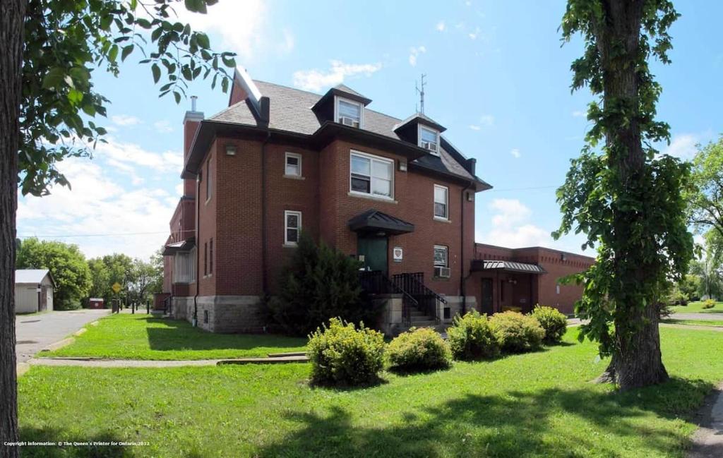 a large red brick house with a green lawn at Wardens Quarters: 2 Bedroom Apt in Sault Ste. Marie