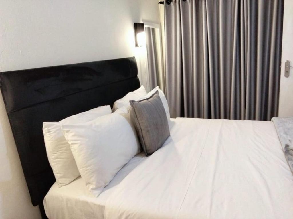 a bedroom with a bed with white sheets and pillows at Tiah Grey, Durban in Durban