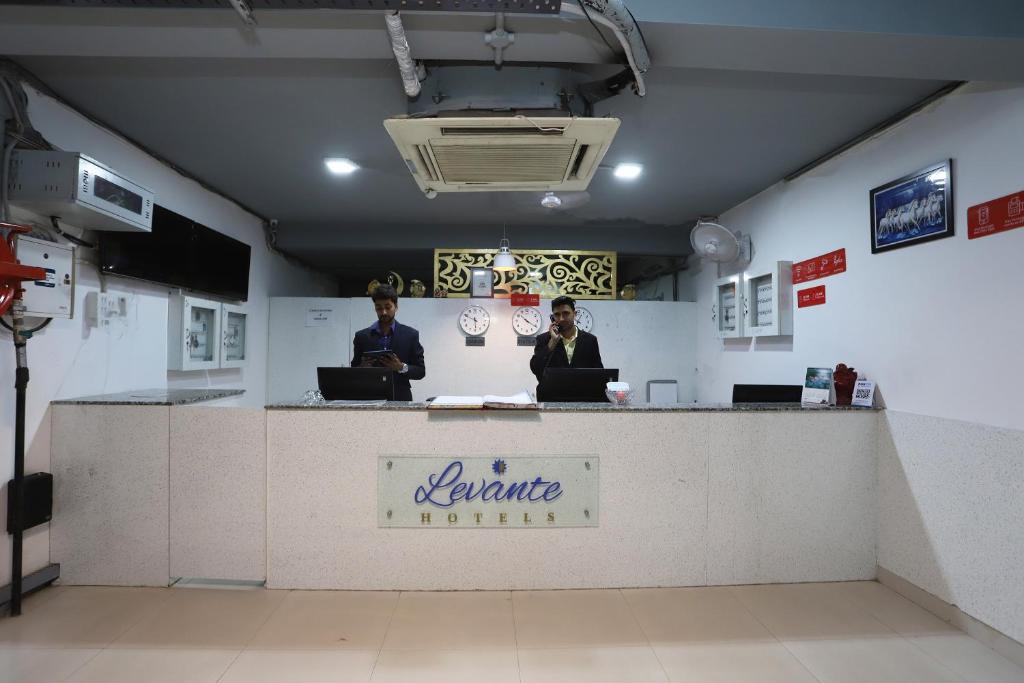 two people standing at a counter with their laptops at Capital O Levanti Near Aravali Biodiversity Park in Gurgaon