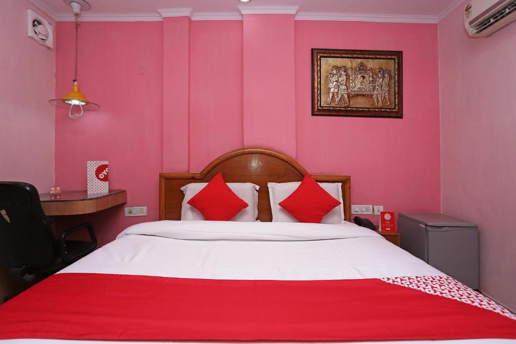 a bedroom with pink walls and a bed with red pillows at Hotel O Madhur Regency in Meerut