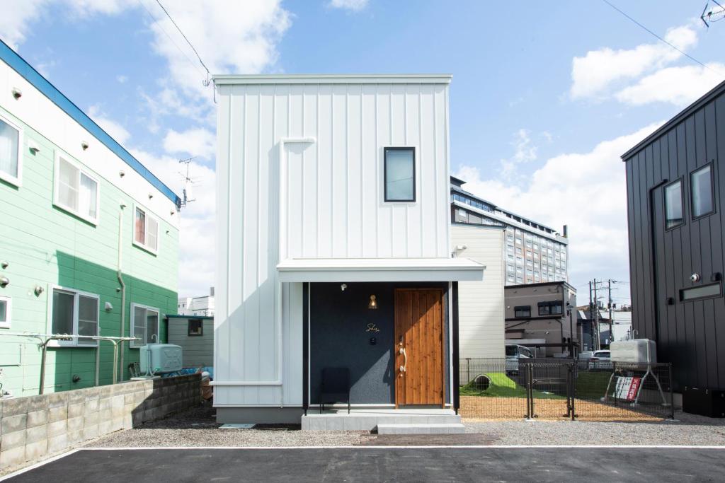 a white house with a wooden door in between two buildings at Shiro in Hakodate