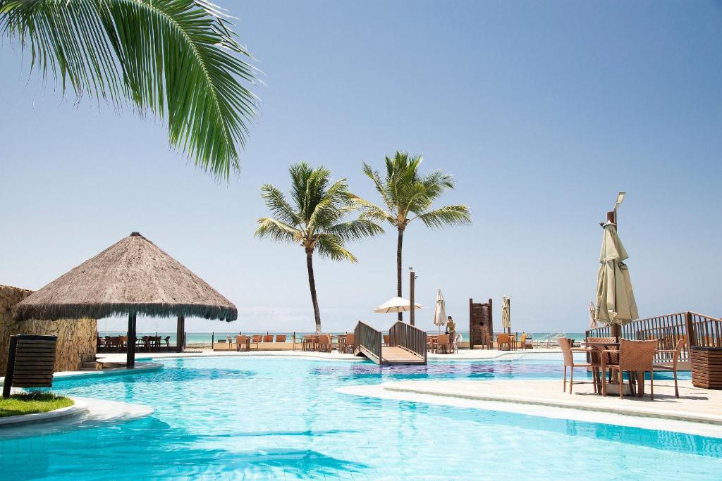 a swimming pool with chairs and palm trees at Pé na areia - verdadeiro paraíso em Muro Alto in Porto De Galinhas