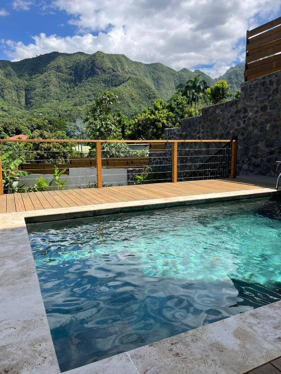 a swimming pool with a deck and mountains in the background at L'échappée de Bras Long in Entre-Deux