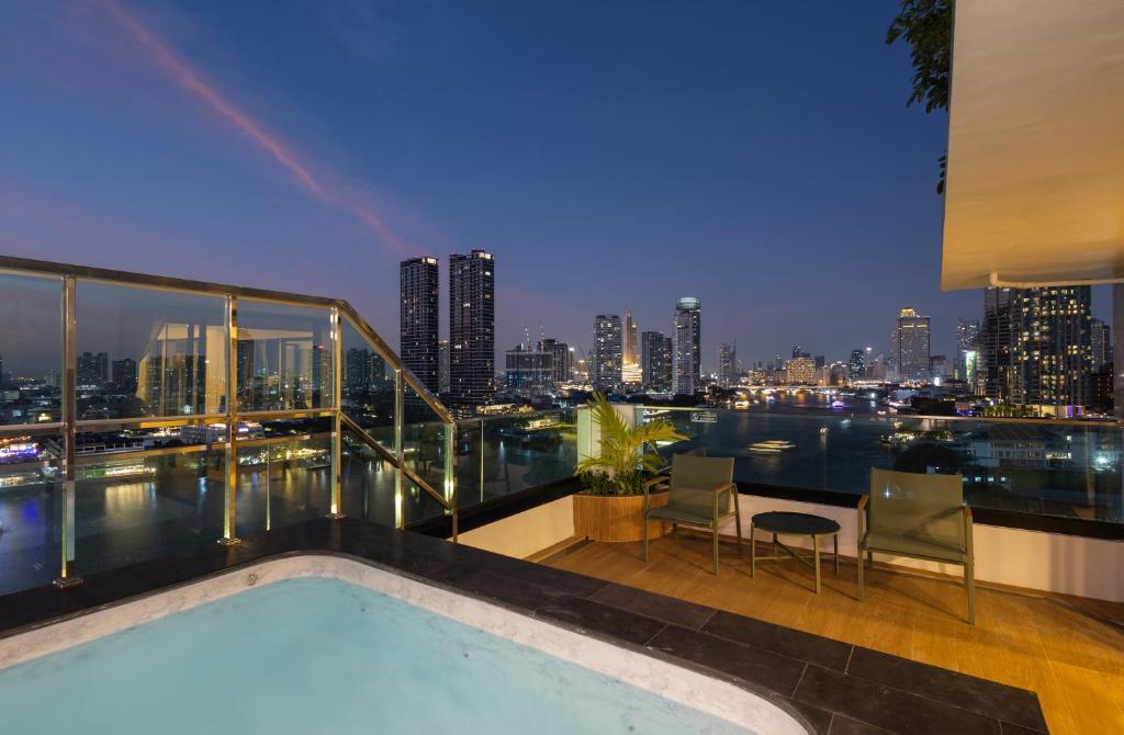 An illuminated rooftop pool terrace overlooking the river and Bangkok skyline at dusk.