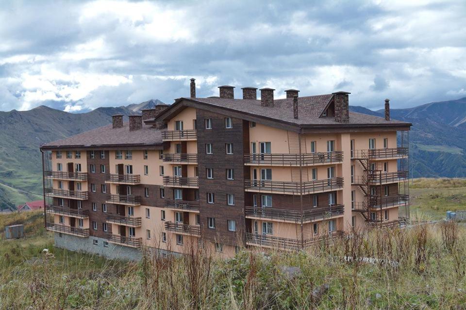 a large building on a hill with mountains in the background at Magi Style - Cosy Flat #5 in Gudauri