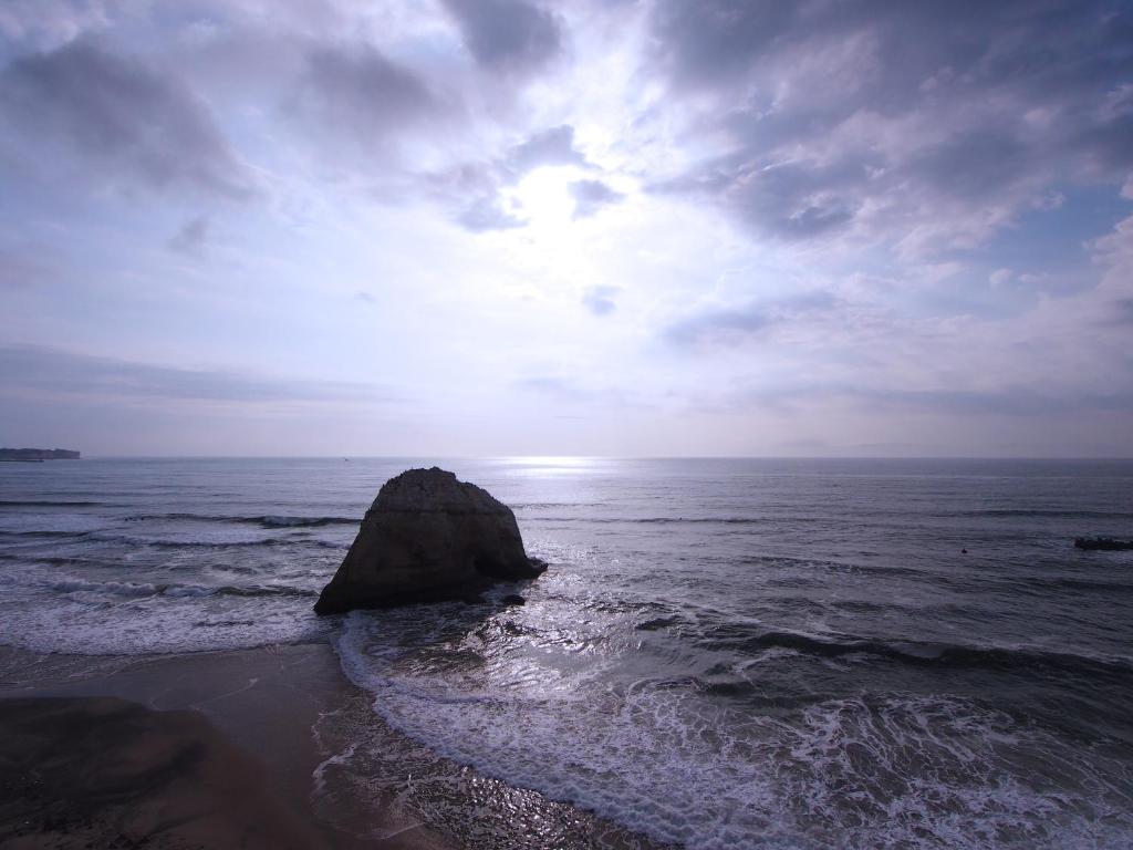 a beach with a rock in the ocean with the sun at Isohara Seaside Hotel in Isohara
