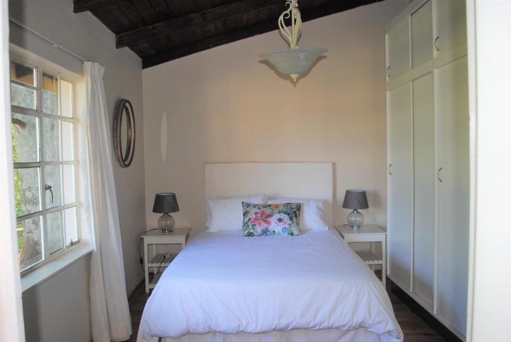 a bedroom with a white bed and two windows at 37 Valley View Cottage in Underberg