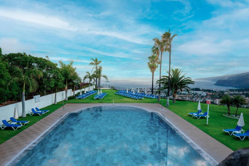 a pool on the roof of a resort with palm trees and chairs at Hotel Las Águilas Tenerife, Affiliated by Meliá in Puerto de la Cruz