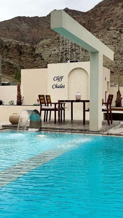a pool with a table and chairs next to a building at Cliff Chalet-Amrat in Al Amarat