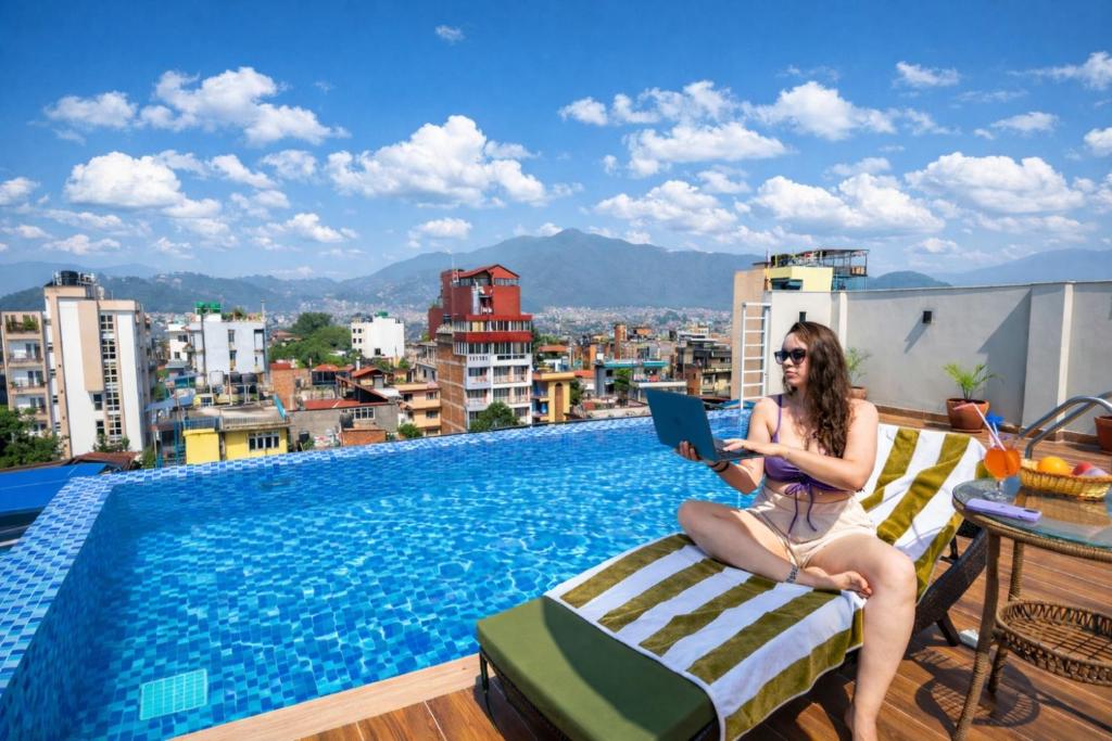 a woman sitting on a chair next to a pool with a laptop at Divine Kathmandu Hotel in Kathmandu