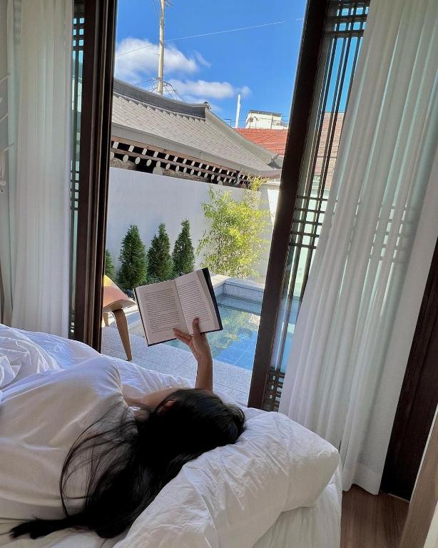 a woman laying on a bed reading a book at 안동 108한옥 in Andong