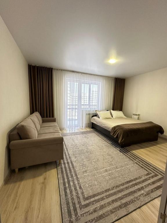 a bedroom with a bed and a couch and a window at Apartment on Satpayeva in Ustʼ-Kamenogorsk
