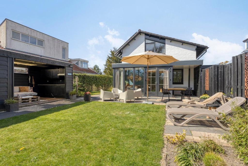 a patio with chairs and an umbrella in a yard at Groenendijk Verhuur Vakantiewoning Casa Iris in Burgh Haamstede