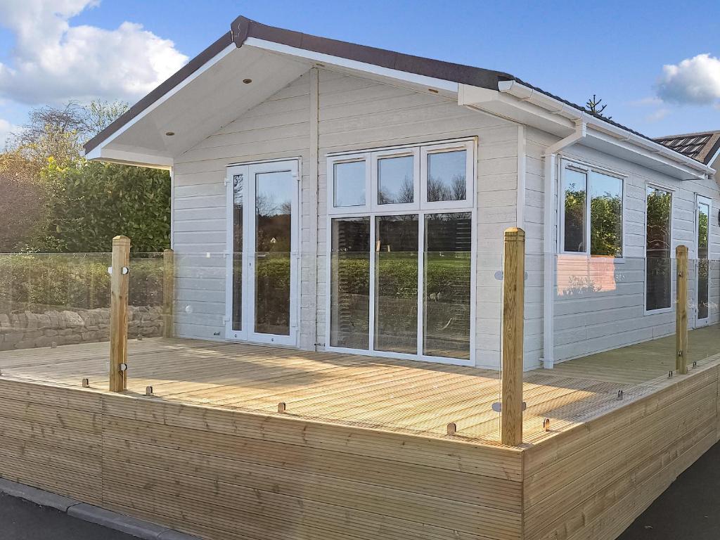 a small white house with a wooden deck at Forrest Lodge in Plumbland