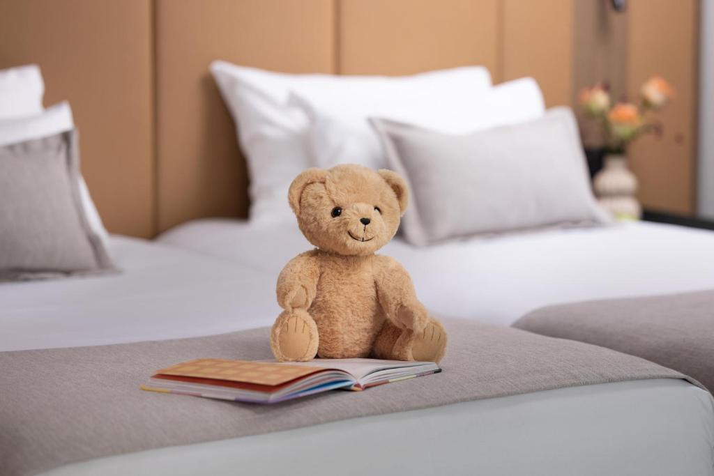 a teddy bear sitting on a bed with a book at NH City Centre Amsterdam in Amsterdam