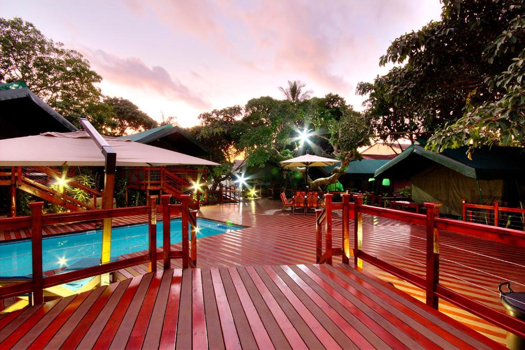 a wooden deck with a pool and tables and umbrellas at Luxury Tented Village @ Urban Glamping in St Lucia