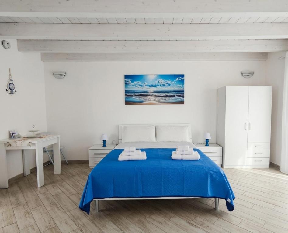 a white bedroom with a blue bed and a table at Sole & Luna in Elmas
