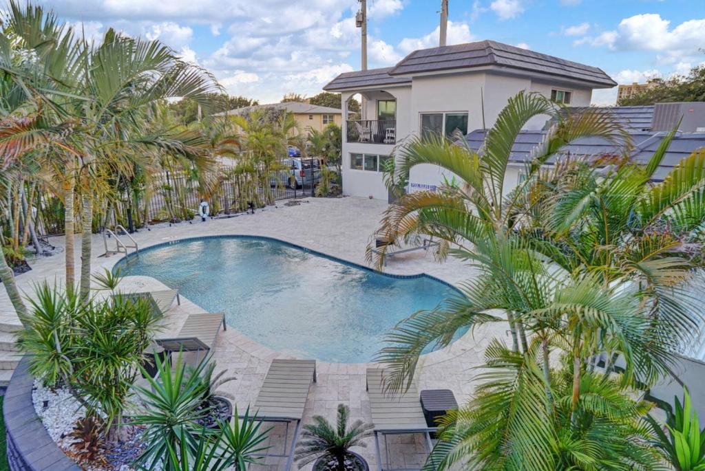 a swimming pool with palm trees in front of a house at Beachside Studio w Pool Access Steps from the Shore in Pompano Beach