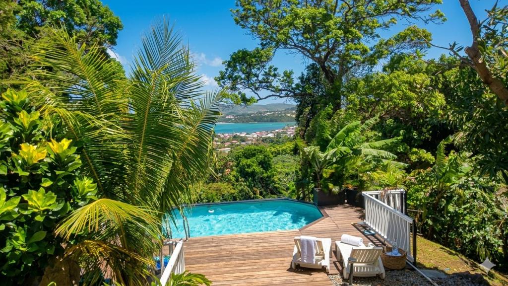 a pool on a wooden deck with a view of the ocean at Douceur de Fèves - T2 de Charme avec Piscine et vue mer à la Trinité in La Trinité