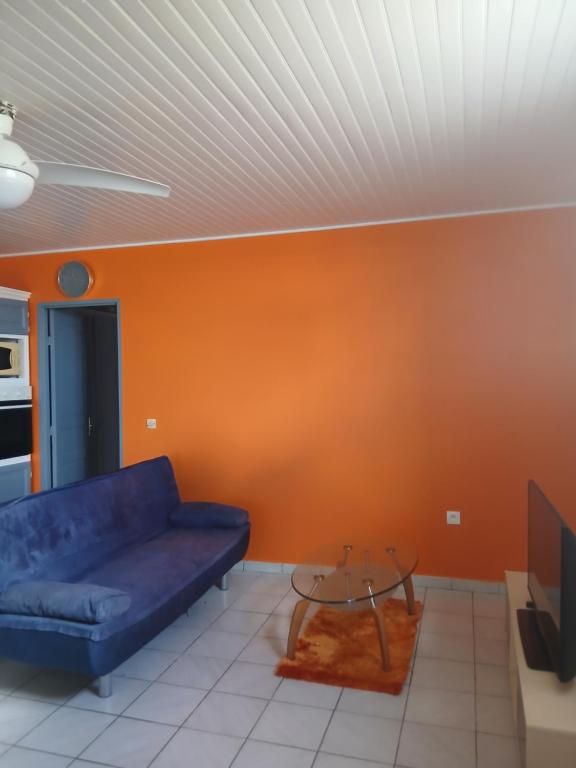 a living room with a blue couch and an orange wall at La vallée verte Martinique in Le Lamentin