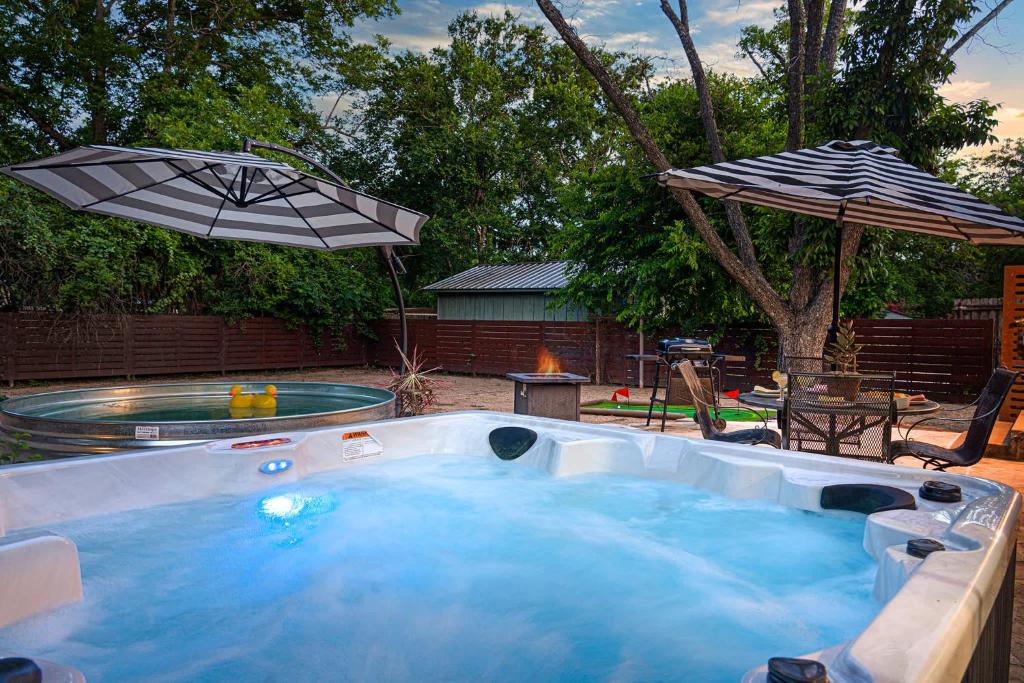 a hot tub with an umbrella in a backyard at Cava House, Hot tub, Cowboy Pool, Fire pit! in Fredericksburg