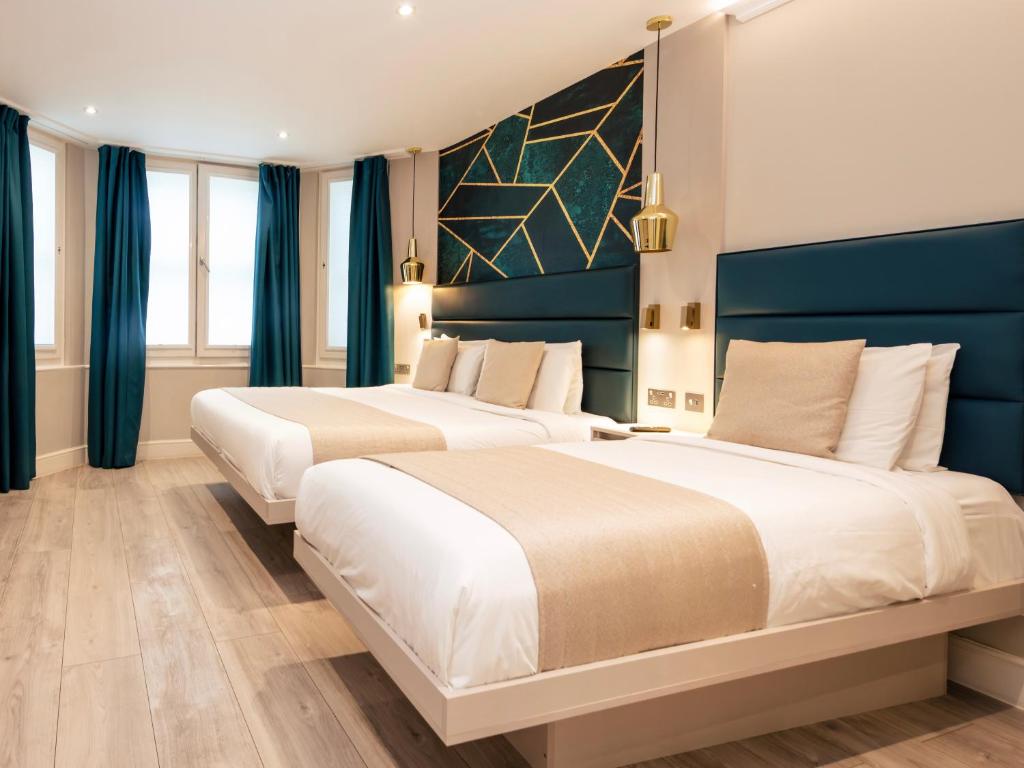 two beds in a hotel room with blue curtains at NOX Kensington in London