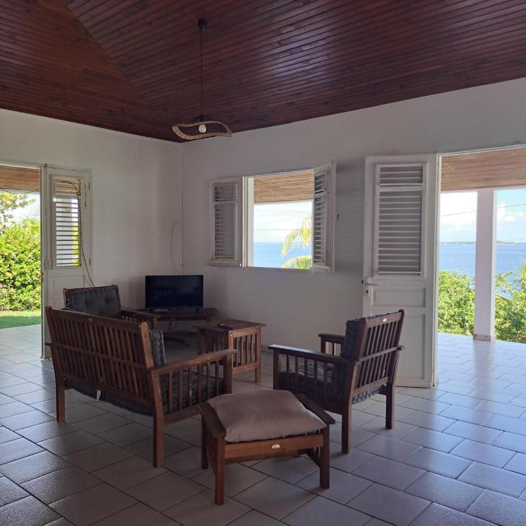 a living room with chairs and a table and windows at La Maison Rose in Le Robert