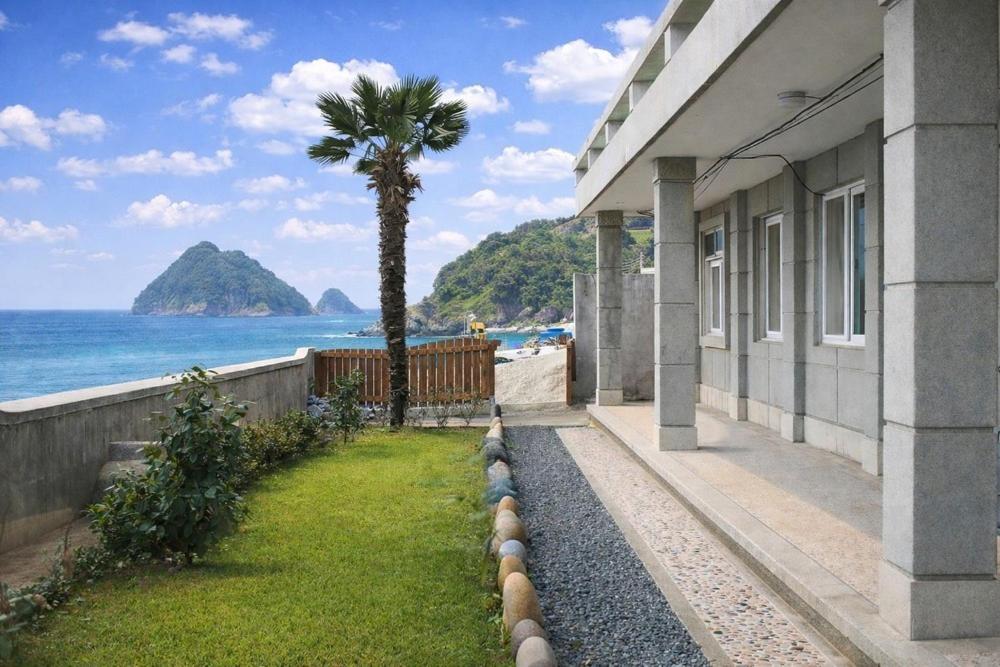 a building with a palm tree next to the ocean at Namhae Padosori Oceanview Pension in Namhae