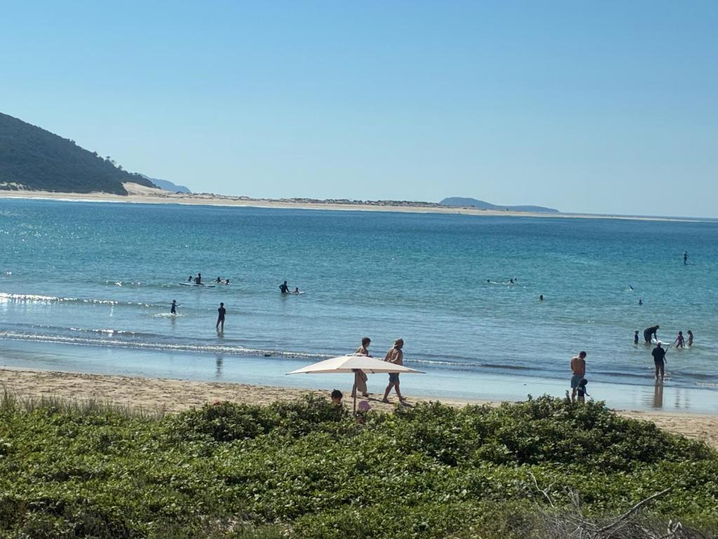 a group of people on a beach with a surfboard at The Mango Tree in Fingal Bay