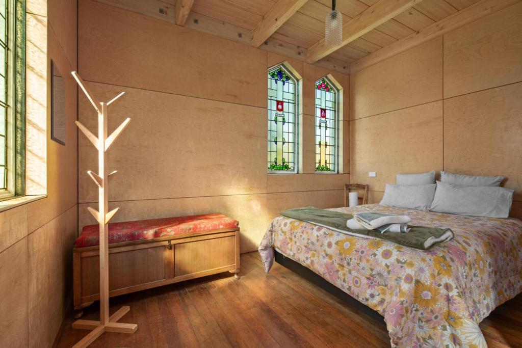 a bedroom with a bed with a bench and two windows at The Church Millers Flat in Millers Flat