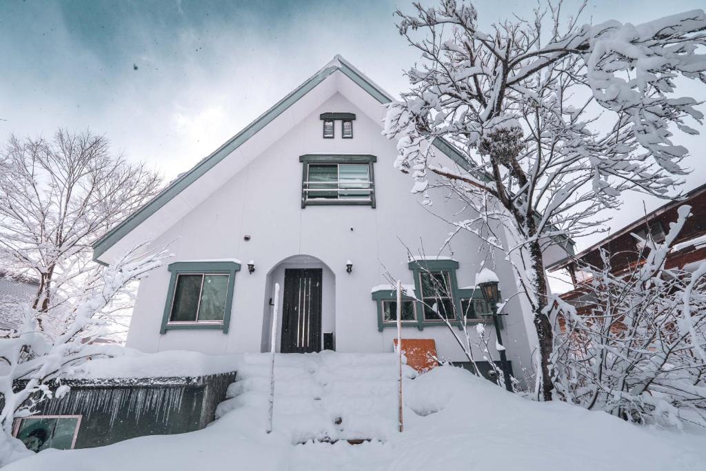 a white house with snow on the ground at Hakuba Slopeside Chalet in Otari