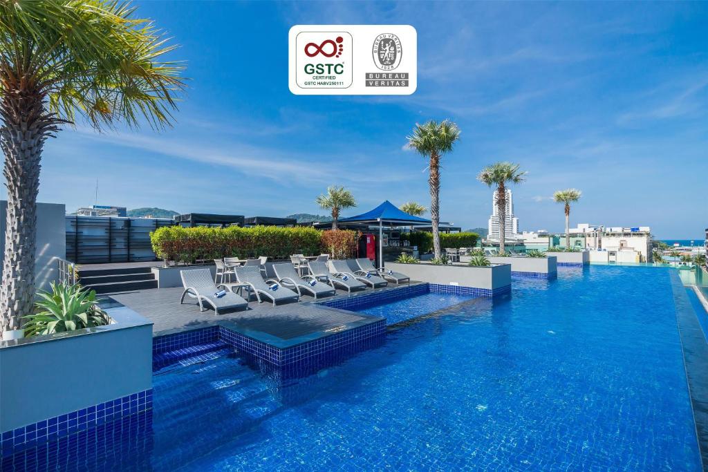 a swimming pool with chairs and palm trees on a building at Best Western Patong Beach in Patong Beach