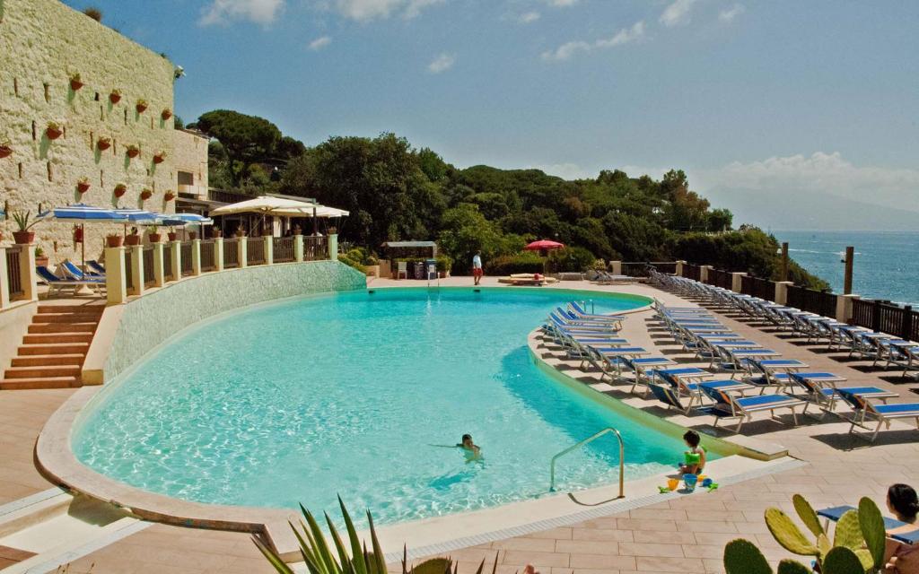 a swimming pool with chairs and people in the water at Baia delle Rocce Verdi Resort in Naples