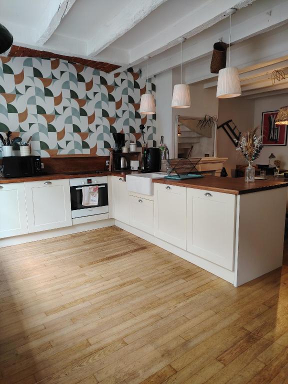 a kitchen with white cabinets and a wooden floor at Nouveau - Maison de charme - Centre de Bourdeilles in Brantome en Perigord
