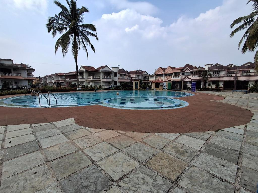 a swimming pool with a palm tree and houses at Bliss Inn in Benaulim