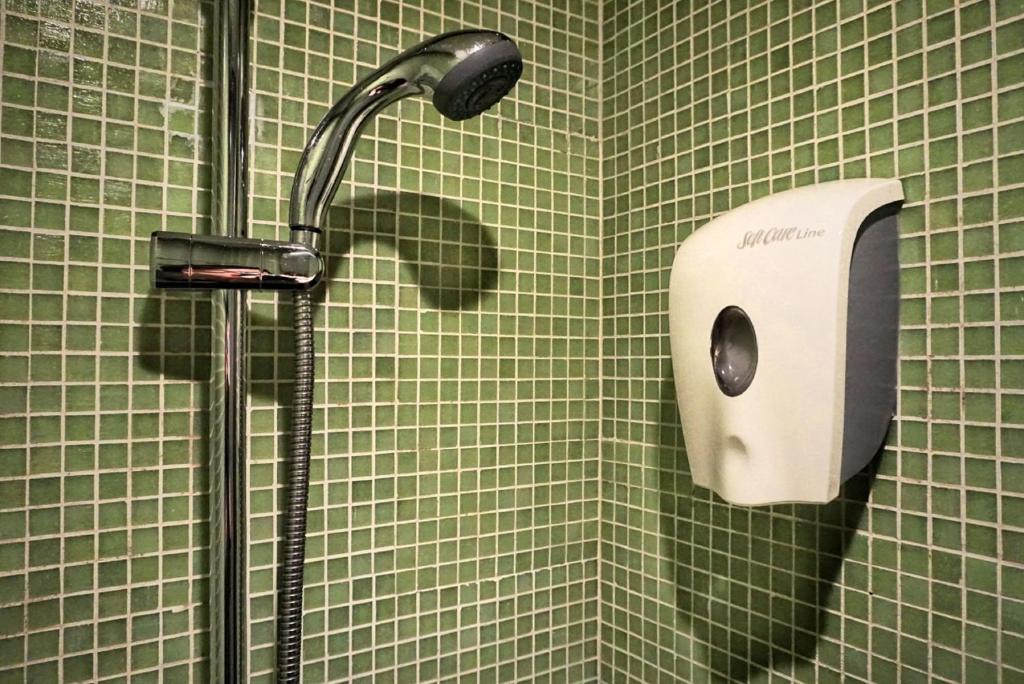 una doccia in un bagno piastrellato verde con un distributore di sapone di Y Loft a Hong Kong