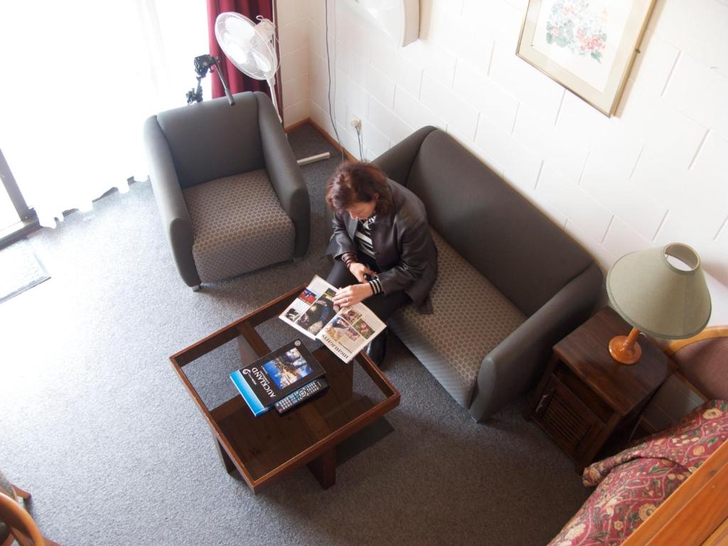 Um homem sentado num sofá a ler uma revista. em New Haven Motel em Auckland