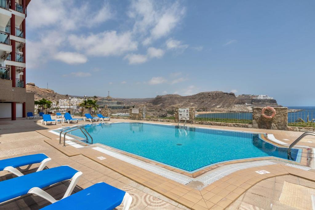 a swimming pool with blue chairs and a building at Su Eminencia in Mogán
