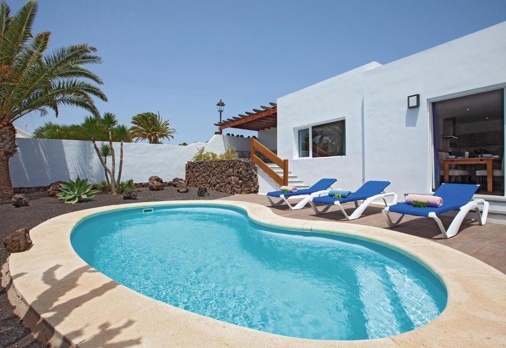 a swimming pool with chairs and a house at Villa Esencia in Puerto del Carmen