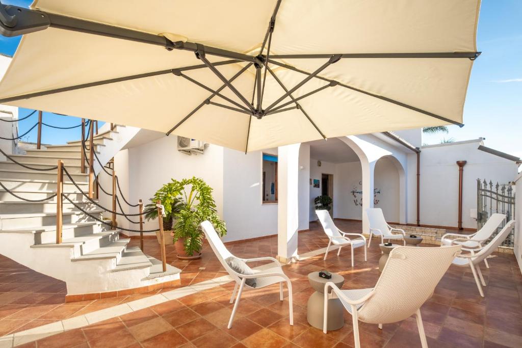 a patio with white chairs and a large umbrella at By The Sea – Le Chele in Torre Lapillo
