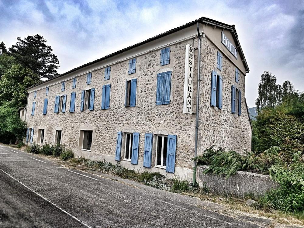 an old stone building with blue shutters on a street at Hôtel Restaurant L'Orée du Vercors in Montmaur-en-Diois
