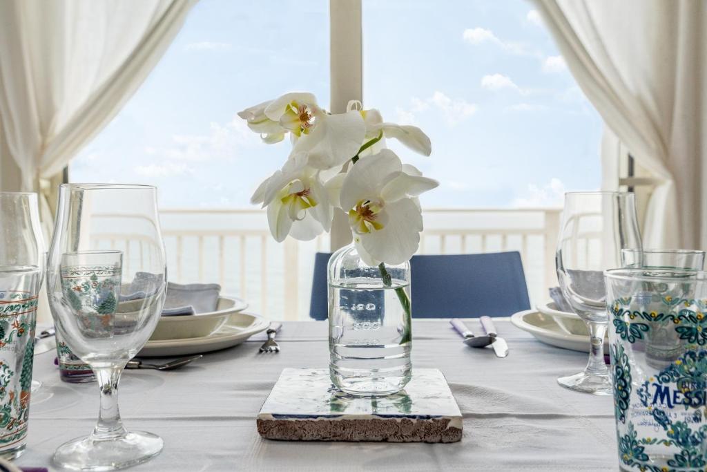 a table with glasses and a vase with flowers in it at Sunset Dimora in Siculiana Marina