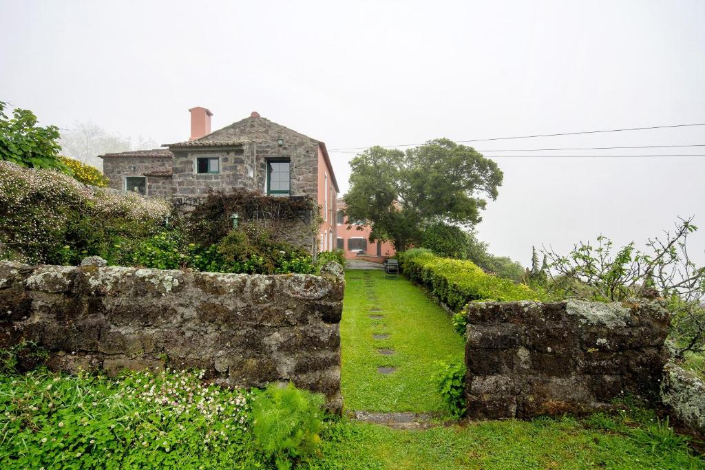 an old stone wall with a house in the background at Quinta das Queimadas in Nordeste
