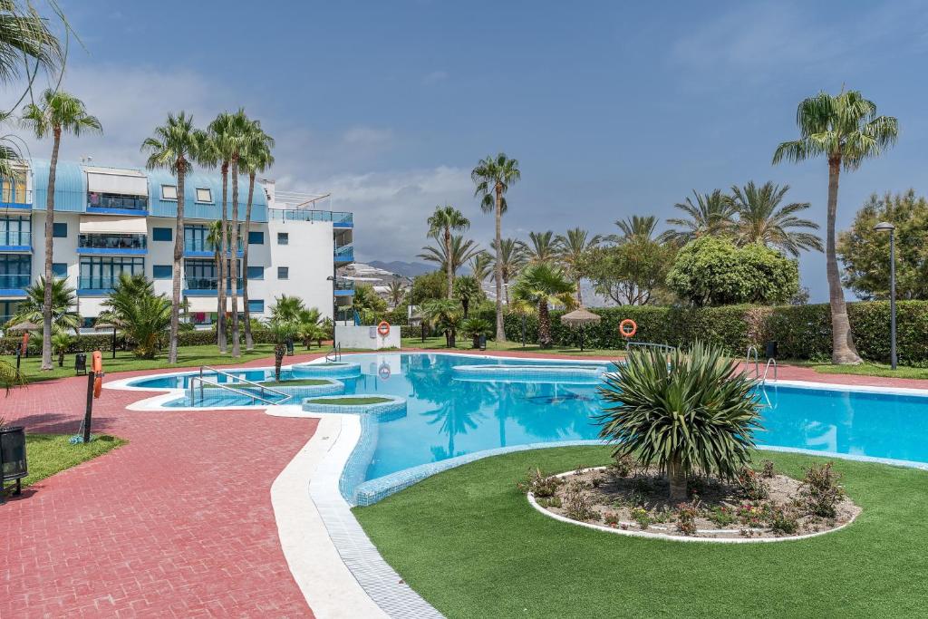 a swimming pool with palm trees and a building at Piso Castell in Castell de Ferro