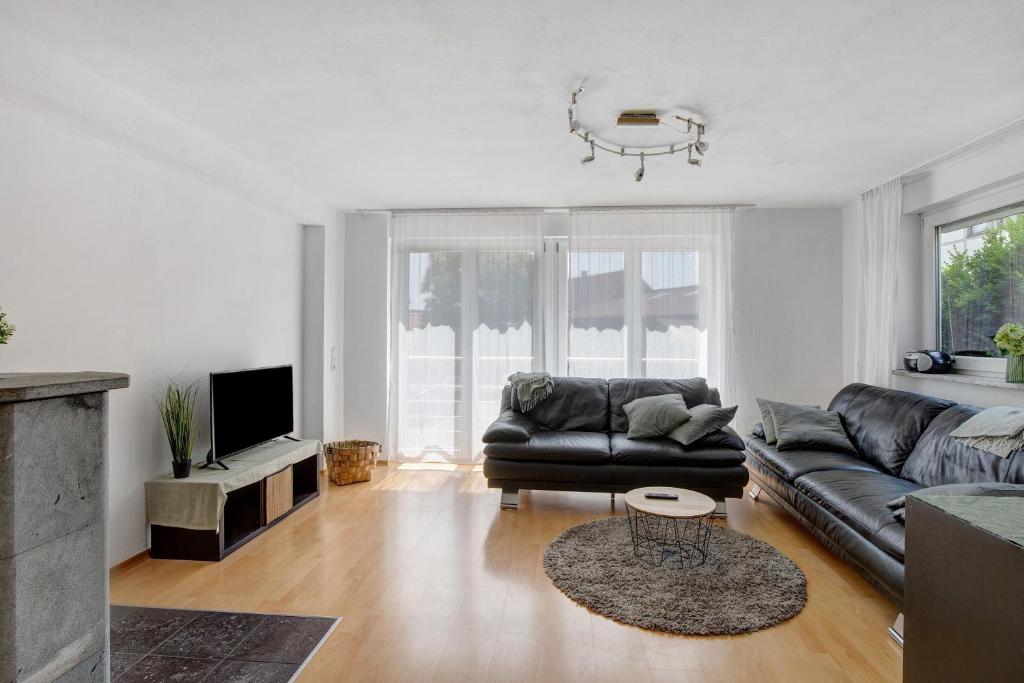 a living room with a black leather couch and a tv at Ferienwohnung am Hof in Zwiefalten