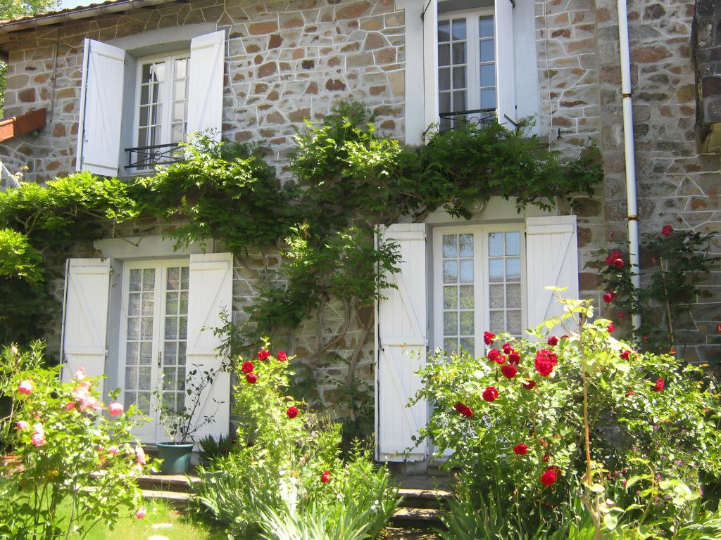 a stone house with white windows and red flowers at Appartement T3 chambre d'hôte in Panazol