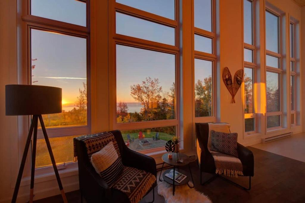 a living room with large windows with chairs and a table at O Vitre Spa - Relax with St-Lawrence Views in Les Éboulements