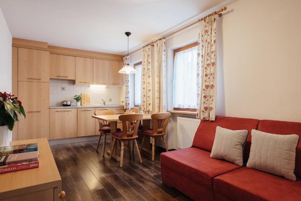 a living room with a red couch and a kitchen at Ciasa Willy App Sas La Crusc in La Villa